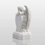 White marble tombstone carved with angel, roses and central blank heart stands on the black gravel cemetery ground.