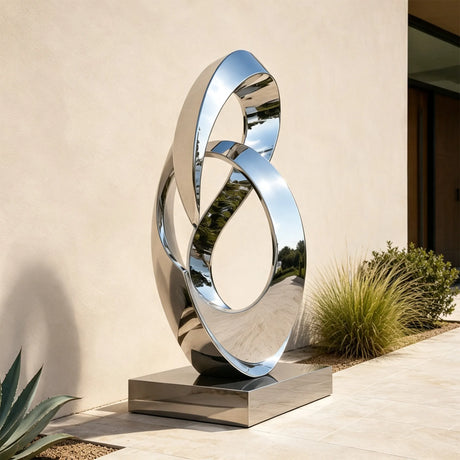A stainless steel intertwined loop sculpture stands beside a walkway in front of a building.