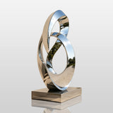 A stainless steel intertwined loop sculpture stands beside a walkway in front of a building.