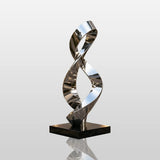 A shiny stainless steel sculpture with infinity loop design stands on paved ground outside a building.