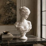White marble female bust statue sits on a dark marble table in a refined indoor room.