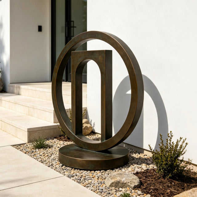 The geometric bronze sculpture stands in gravel planting bed near a home entrance.