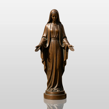 The bronze our lady of grace statue stands outdoors beside stone walkway near a church.