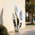 A stainless steel leaf sculpture sits beside a light stone building in the afternoon.
