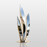 A stainless steel leaf sculpture sits beside a light stone building in the afternoon.