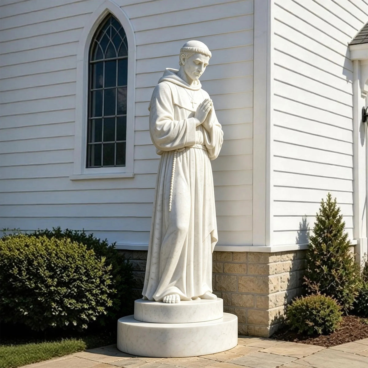 A Saint Francis of Assisi statue in white marble stands on the base beside a house.