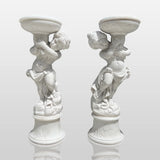 Pair of marble sculptures depicting children holding flowerpots line a curved gravel garden path beside trimmed hedges and rose blooms.