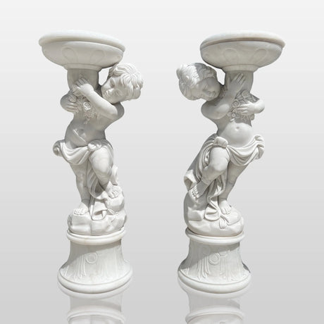 Pair of marble sculptures depicting children holding flowerpots line a curved gravel garden path beside trimmed hedges and rose blooms.