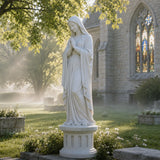 Marble Virgin Mary statue stands on green grass beside a church.