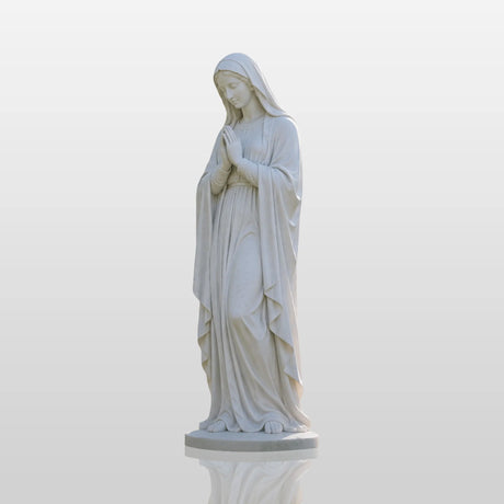 Marble Virgin Mary statue stands on green grass beside a church.
