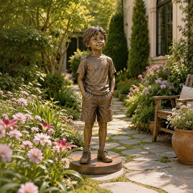 Lifelike bronze statue of a young boy stands along stone stepping walkway in a private garden.