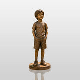 Lifelike bronze statue of a young boy stands along stone stepping walkway in a private garden.