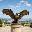 A large bronze eagle statue stands on a pedestal overlooking a valley and town.