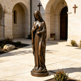 A bronze Virgin Mary statue stands on the paving inside an arched church courtyard.