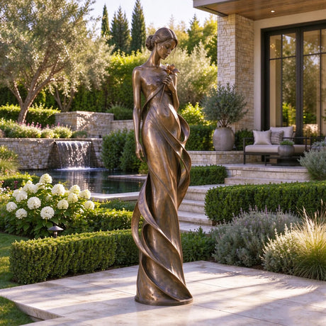 Bronze lady statue with a flower stands on stone patio amid lush landscaped greenery.
