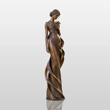 Bronze lady statue with a flower stands on stone patio amid lush landscaped greenery.