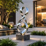 Polished stainless steel ribbon sculpture rests beside a garden water pond.