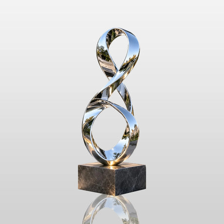 Polished stainless steel ribbon sculpture rests beside a garden water pond.