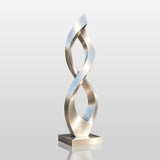A brushed stainless steel infinity sculpture stands on paved ground outside a modern house.