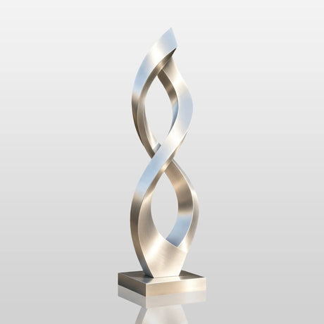 A brushed stainless steel infinity sculpture stands on paved ground outside a modern house.