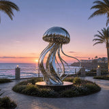 Shiny stainless steel jellyfish statue sits on a coastal flower bed with ocean sunset.