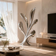Polished stainless steel leaf sculpture stands inside a bright modern living room.