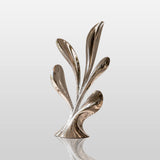 Polished stainless steel leaf sculpture stands inside a bright modern living room.
