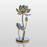 Polished stainless steel lotus sculpture stands on the grassy lake shore under bright sunshine.