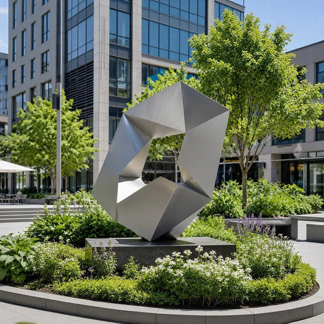 Matte stainless steel geometric sculpture stands in front of modern glass office building.