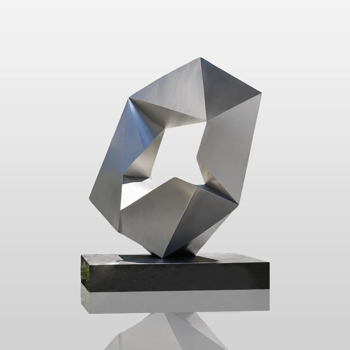Matte stainless steel geometric sculpture stands in front of modern glass office building.