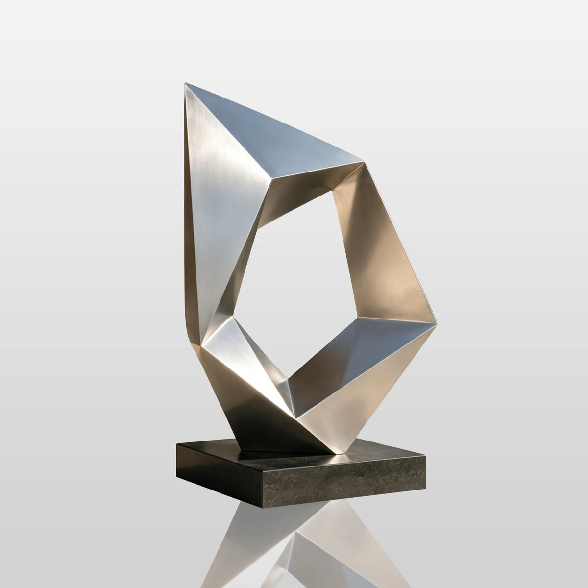 A geometric stainless steel sculpture stands on a dark stone base beside greenery.