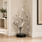 Polished stainless steel abstract leaf sculpture stands in an indoor home corner.