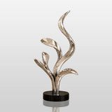 Polished stainless steel abstract leaf sculpture stands in an indoor home corner.