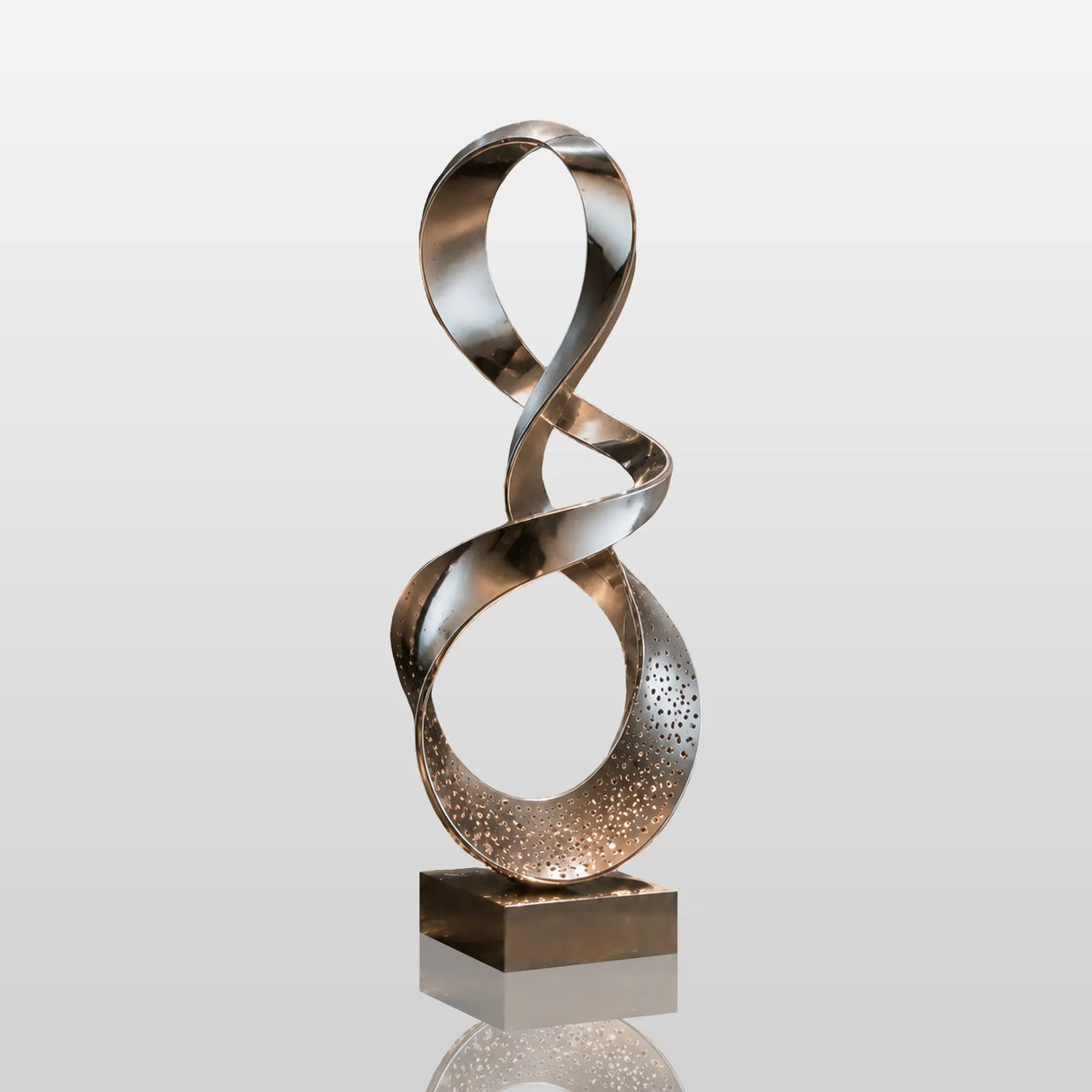 Mirror polished stainless steel ribbon sculpture stands on a square base in dimly lit indoor space.