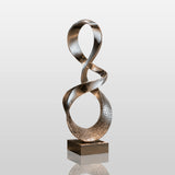 Mirror polished stainless steel ribbon sculpture stands on a square base in dimly lit indoor space.