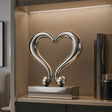 Polished stainless steel heart tabletop sculpture sits inside a display cabinet.