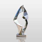 Polished loop stainless steel sculpture stands beside a swimming pool.