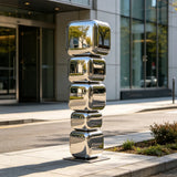 Mirror stacked cube stainless steel sculpture stands on city sidewalk outside a modern building.
