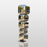 Mirror stacked cube stainless steel sculpture stands on city sidewalk outside a modern building.