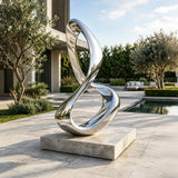 A stainless steel infinity loop sculpture stands on stone base beside a swimming pool.