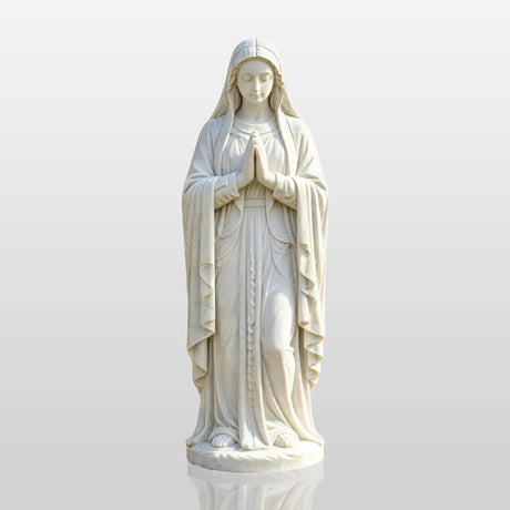 White marble Virgin Mary statue stands on paved circle amid green lawn and trees.