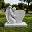 Marble tombstone featuring an angel embracing a heart rests on the cemetery lawn.