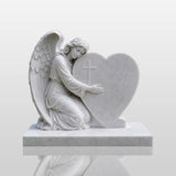 Marble tombstone featuring an angel embracing a heart rests on the cemetery lawn.