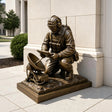 Bronze statue of a kneeling signaller sits outdoors beside a modern building.