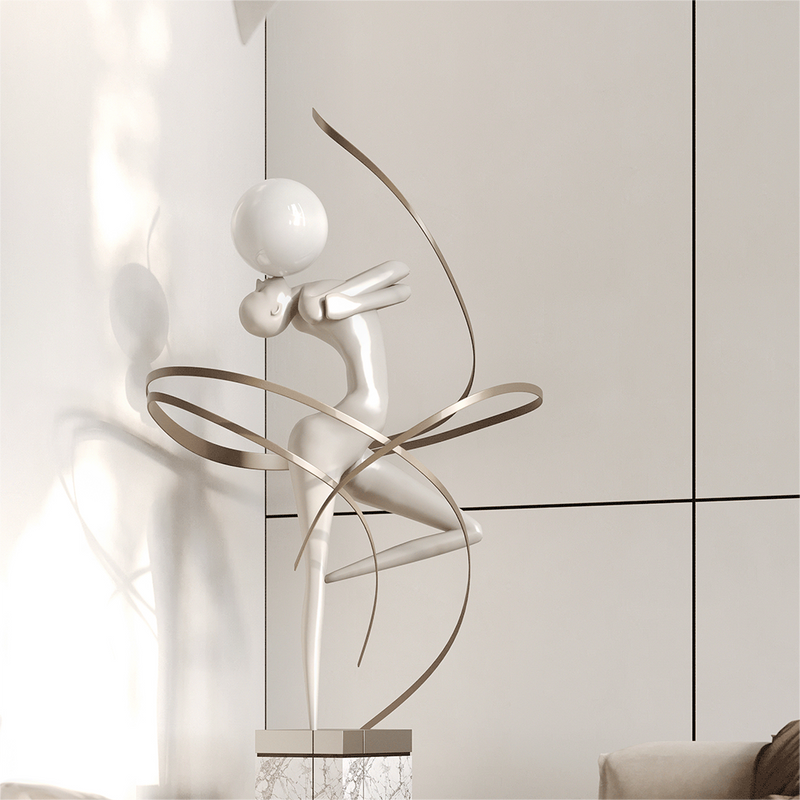 The smooth sculpture is made of white fiberglass. It depicts a figure kissing a white sphere surrounded by a metal ribbon.